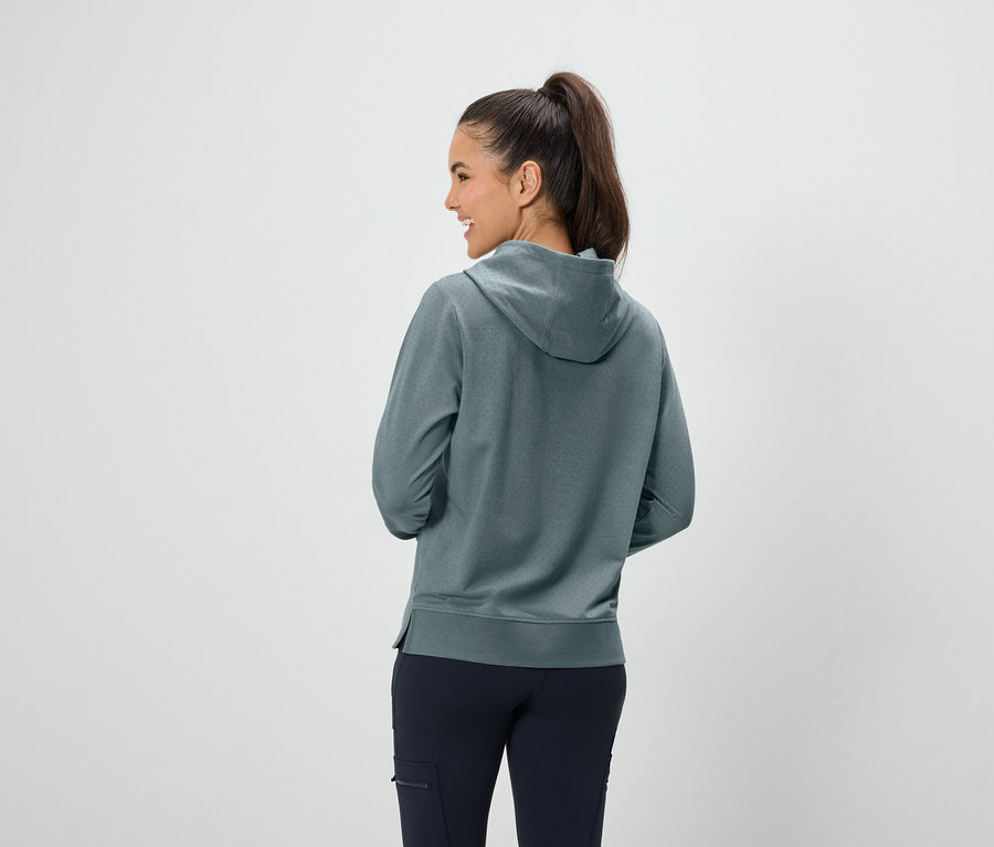 Žena s hnedými vlasmi v cope stojí chrbtom a má na sebe modrozelenú mikinu s kapucňou a tmavomodré nohavice.