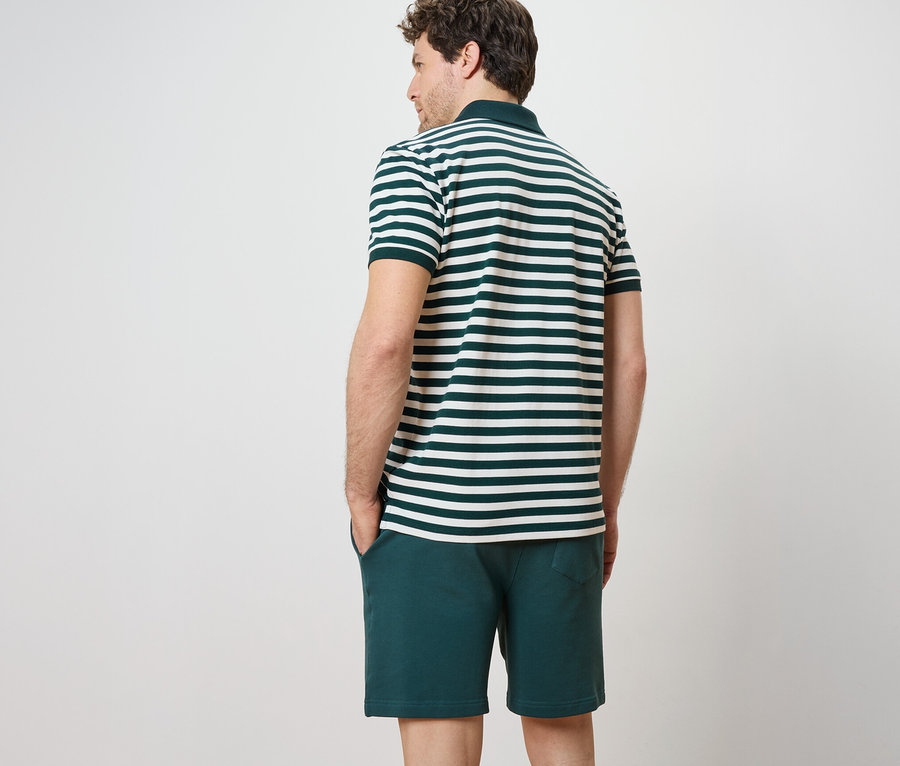 Muž chrbtom k fotoaparátu má na sebe piké polokošeľu s krátkym rukávom a šortky.