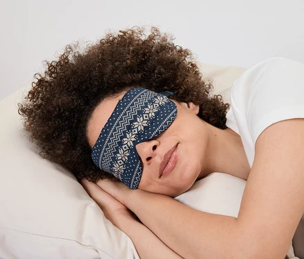 Žena leží na vankúši s modrou maskou na spanie s bielym vzorom.