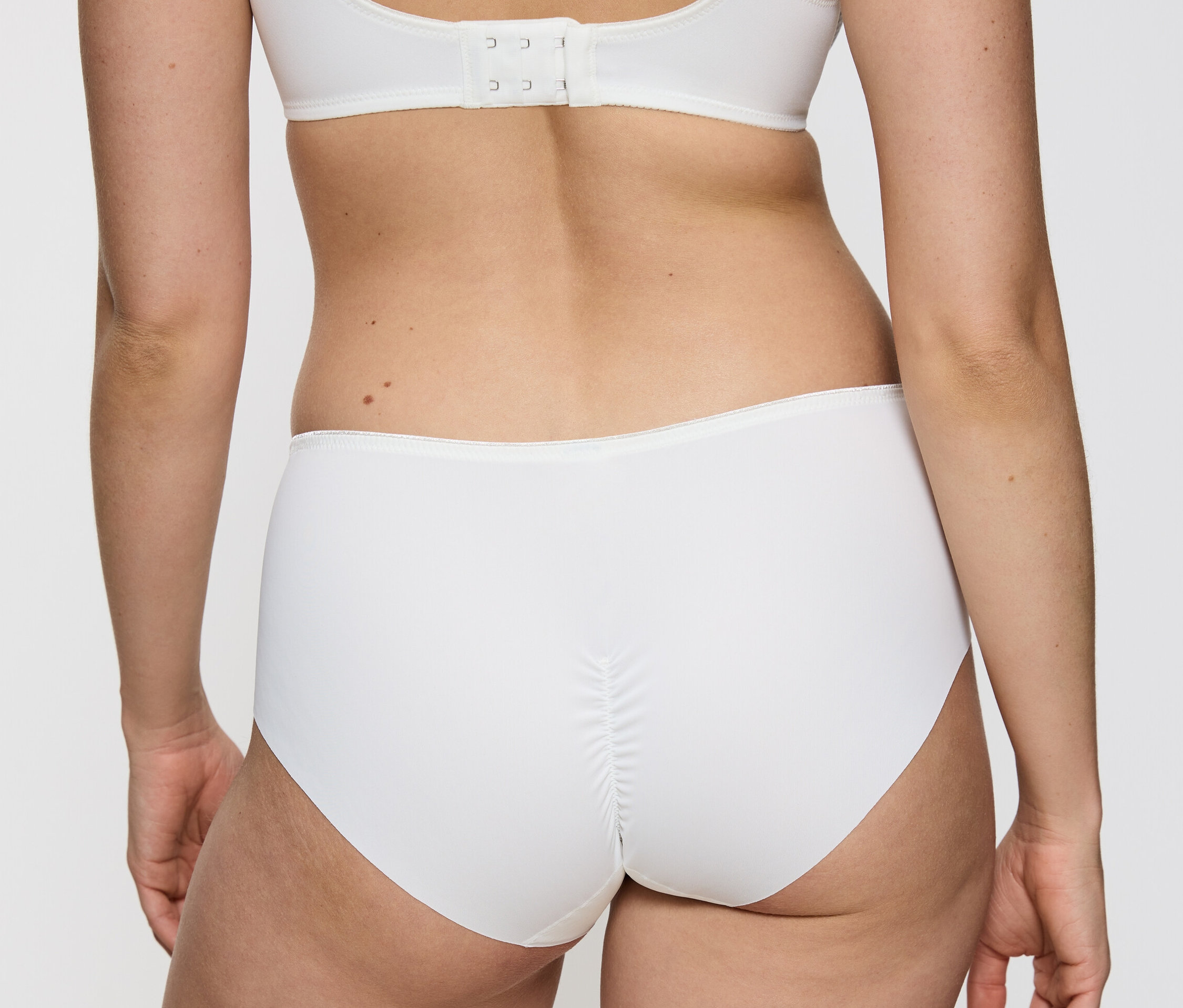 Pohľad zozadu na ženu, ktorá má na sebe biele nohavičky Triumph Essential »Minimizer Hipster X«, vanilkové a bielu podprsenku.