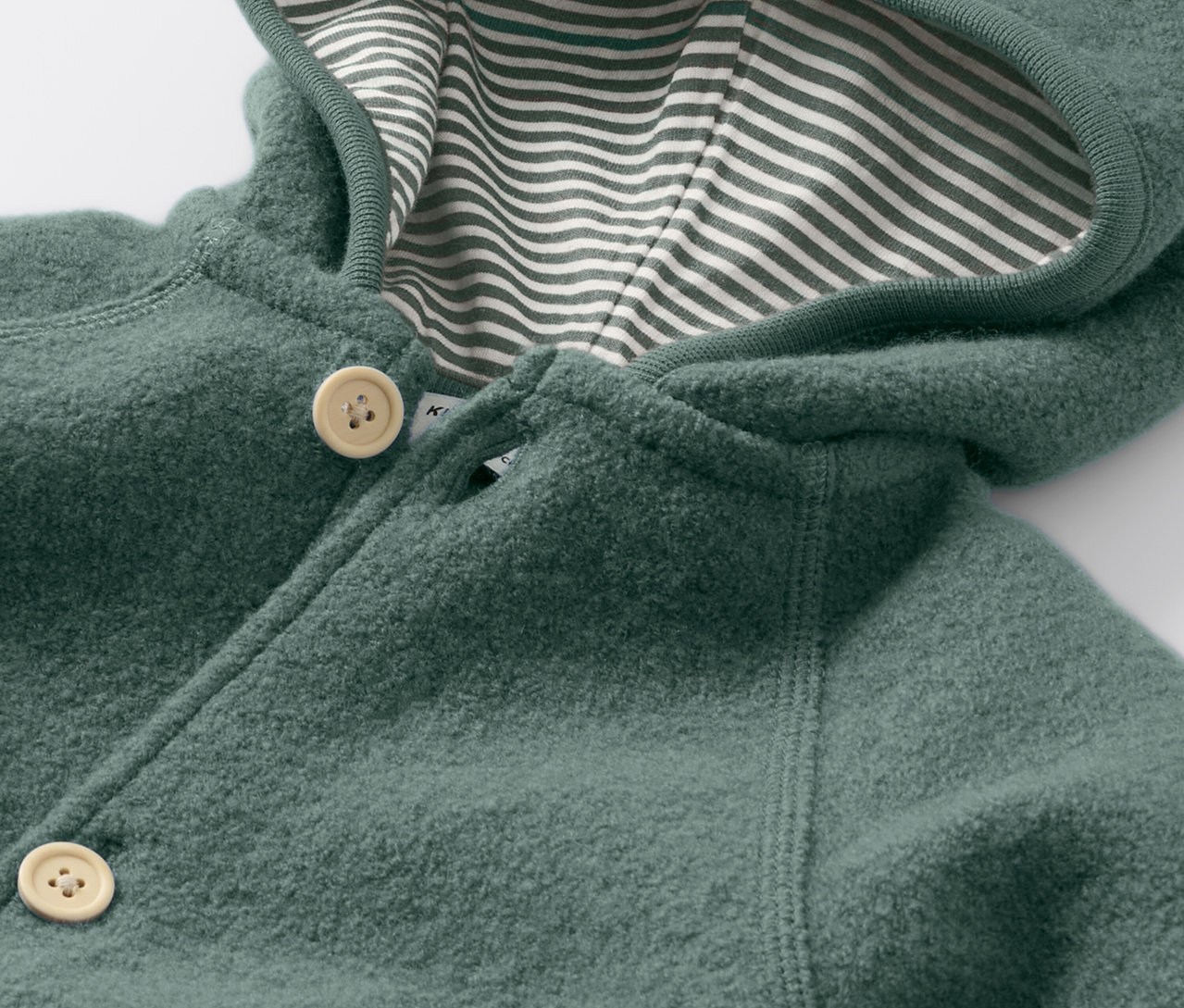 Detailný pohľad na detský vychádzkový overal s vlnou merino, zapínaný na gombíky a s kapucňou s pruhovanou podšívkou.