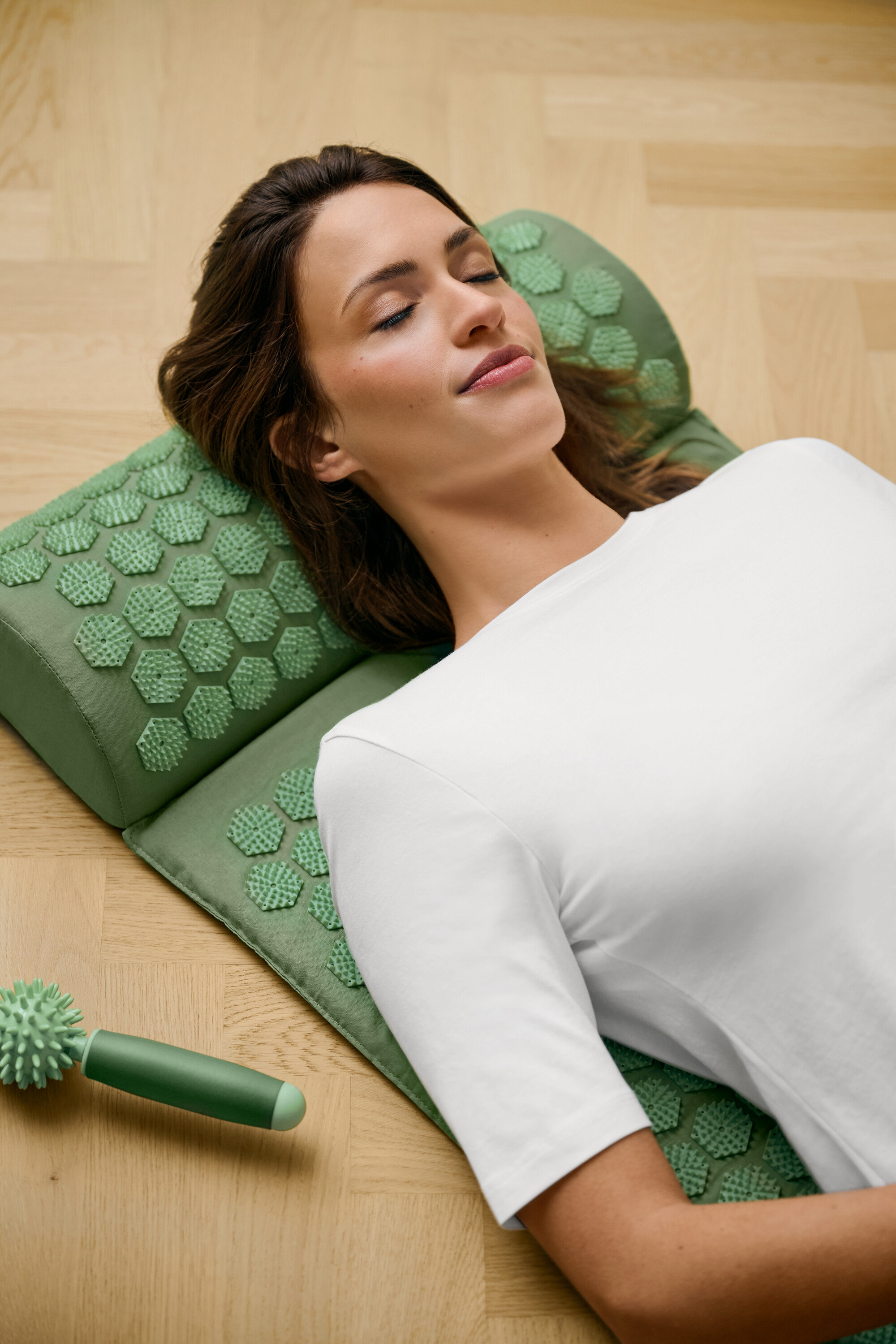 Žena leží na zelenej akupresúrnej podložke a má na sebe biele tričko s polovičným rukávom.