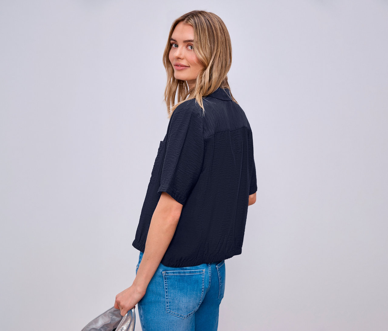 Žena sa pozerá cez plece a má na sebe košeľovú blúzku Street One a džínsy.