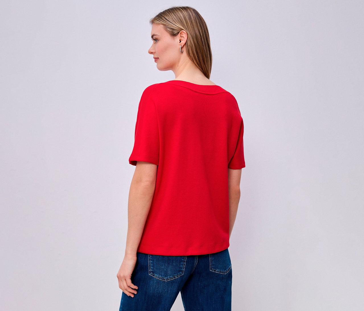 Žena zozadu v červenom tričku s krátkym rukávom Street One a džínsoch.