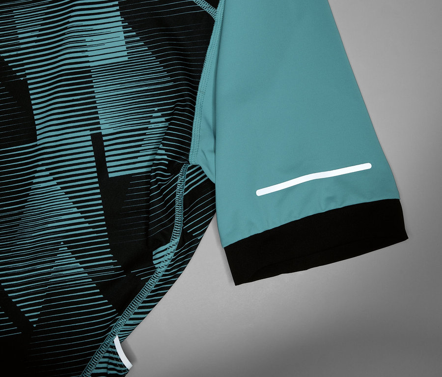 Detail cyklistického dresu s tyrkysovým rukávom, čiernou manžetou a reflexným prúžkom.