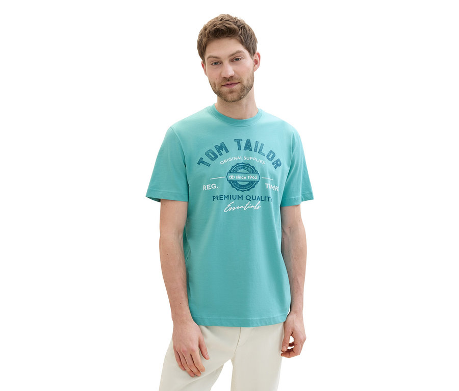 Muž má na sebe tričko Tom Tailor s logom, meadow teal a svetlé nohavice.