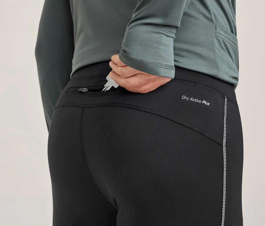 Osoba zozadu vkladá kľúče do zadného vrecka na zips čiernych športových nohavíc. Nohavice majú nápis „Dry Active Plus“ a reflexný pásik.