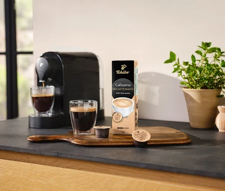 Kávovar naleje kávu do sklenice vedľa balenia kapsúl Cafissimo Decaffeinato.