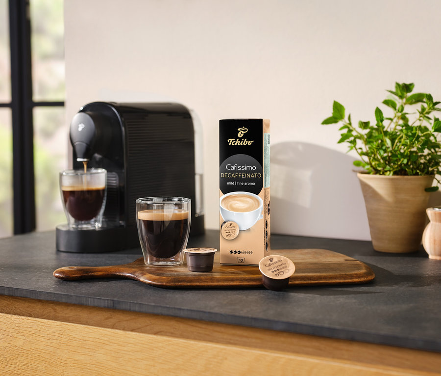 Kávovar naleje kávu do sklenice vedľa balenia kapsúl Cafissimo Decaffeinato.