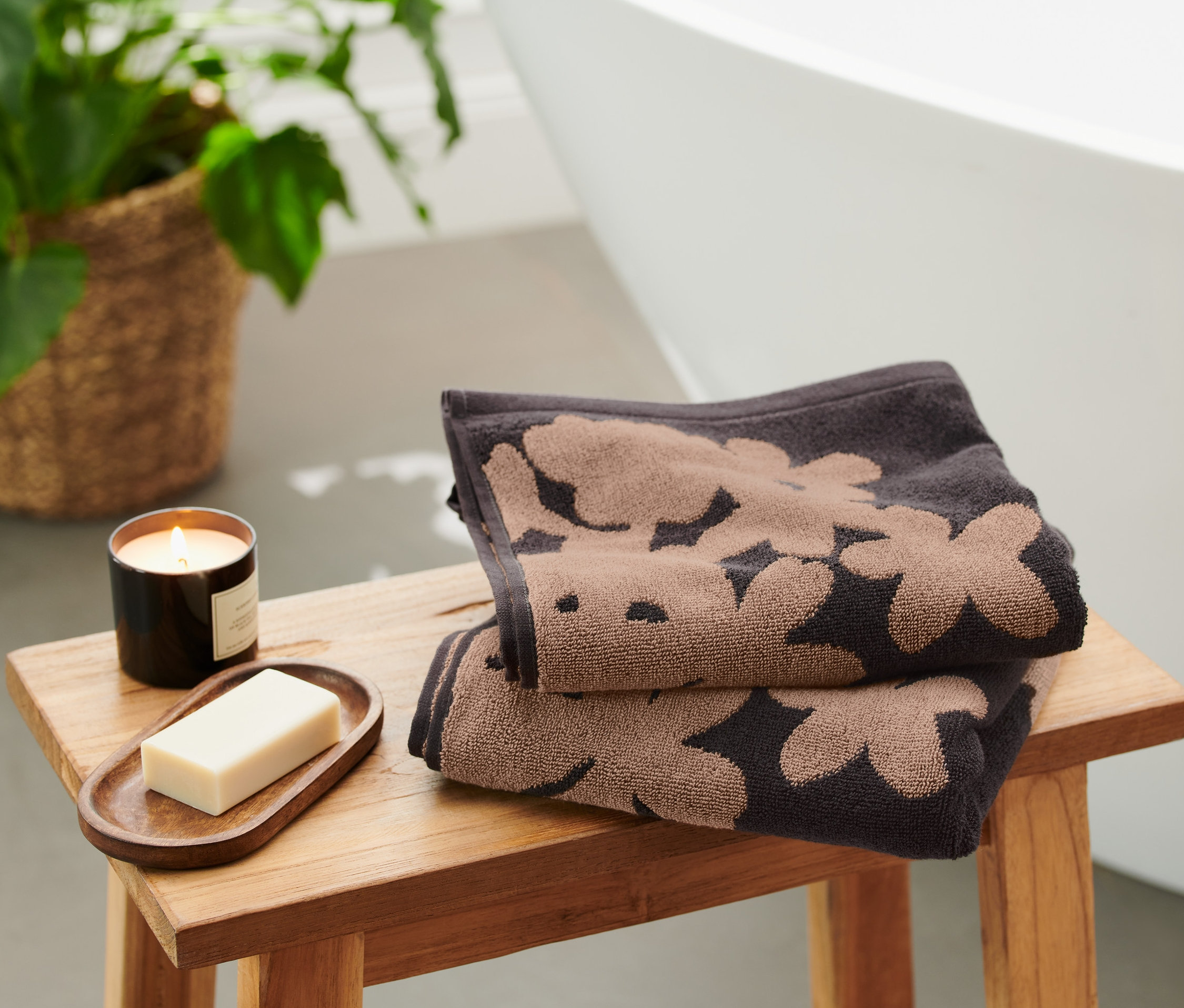 Dva čierne žakárové uteráky s kvetinovým vzorom ležia zložené na drevenej stoličke vedľa sviečky a mydla.