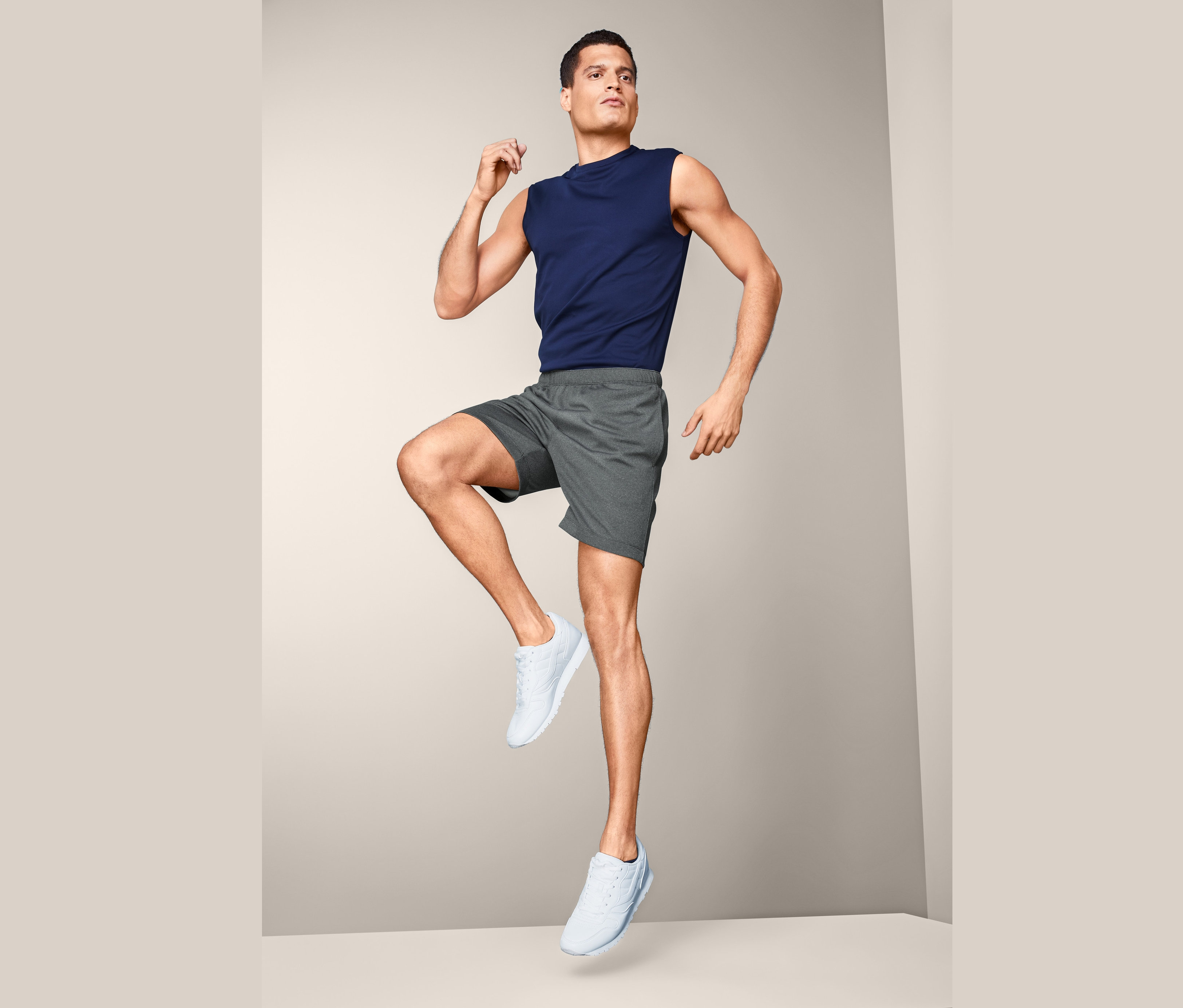 Muž v športových nohaviciach a tielku pózuje v štúdiu.