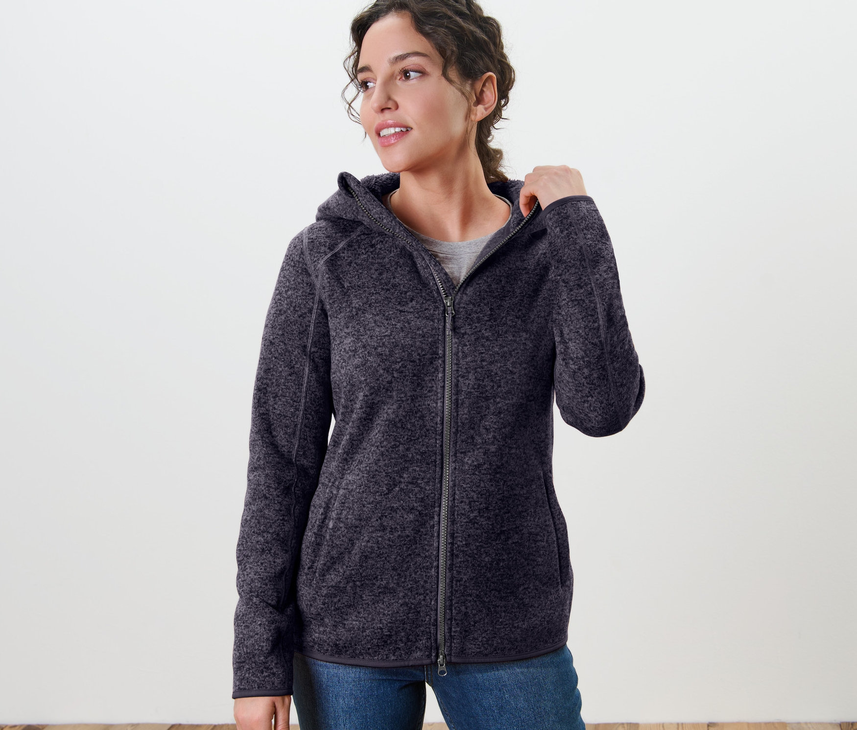 Žena má na sebe bundu z pleteného flísu s kapucňou, tmavomodrá s melírom.