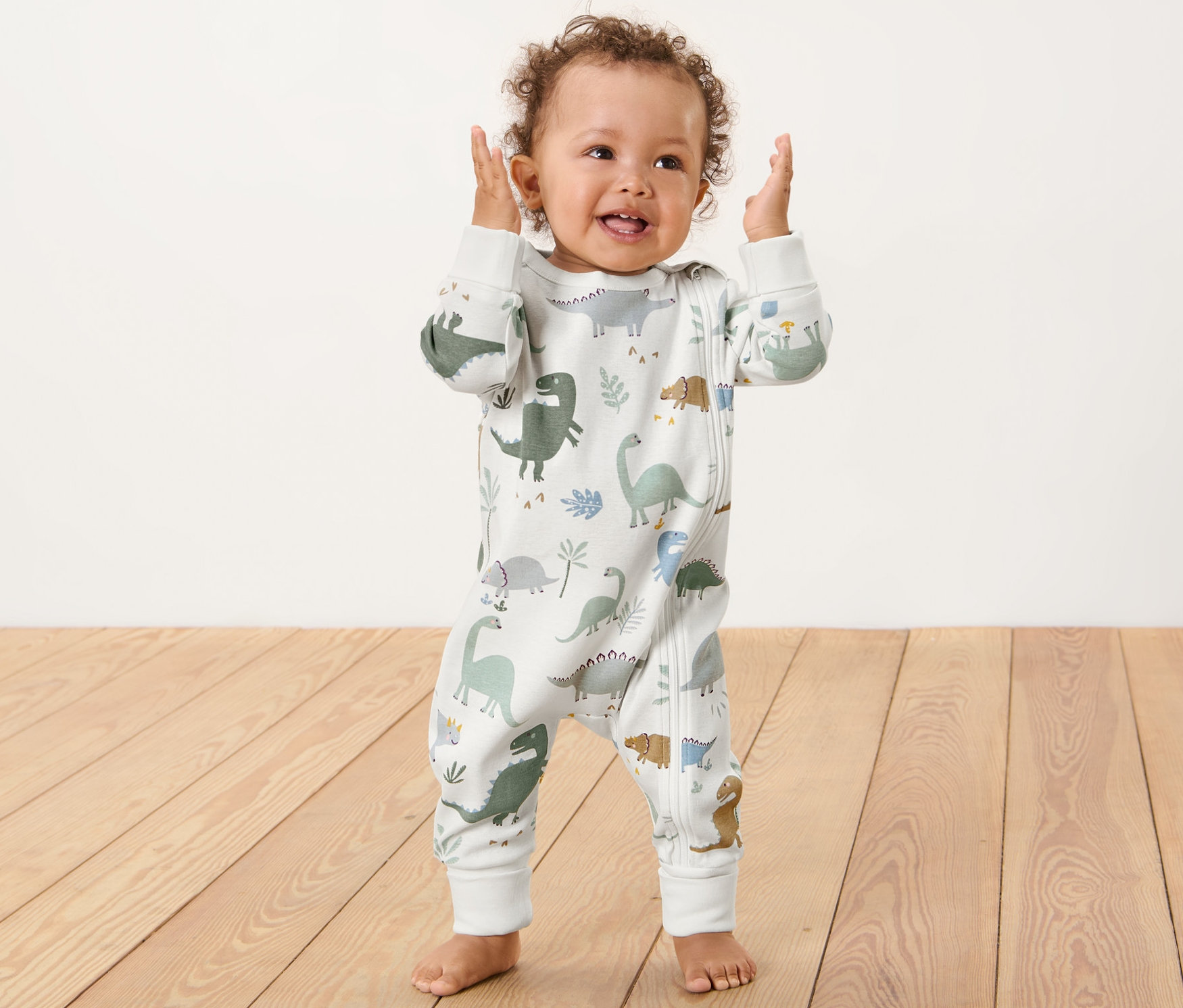 Batoľa stojí a máva rukami. Má na sebe pyžamo s dinosaurami.