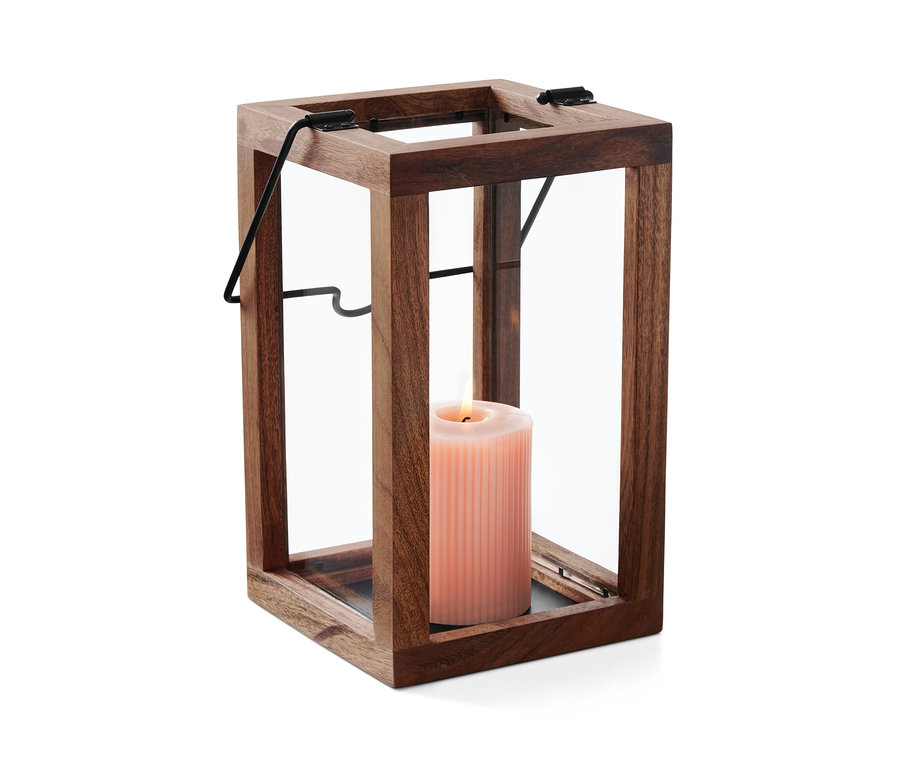 Vo vnútri dreveného svietnika so sklenenými stenami horí ružová sviečka.