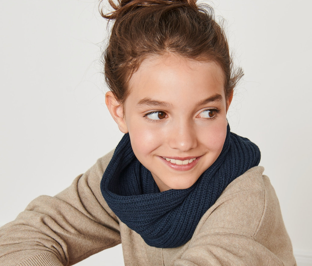 Usmievajúce sa dospievajúce dievča sedí chrbtom k fotoaparátu a má na sebe pletený dutý šál.