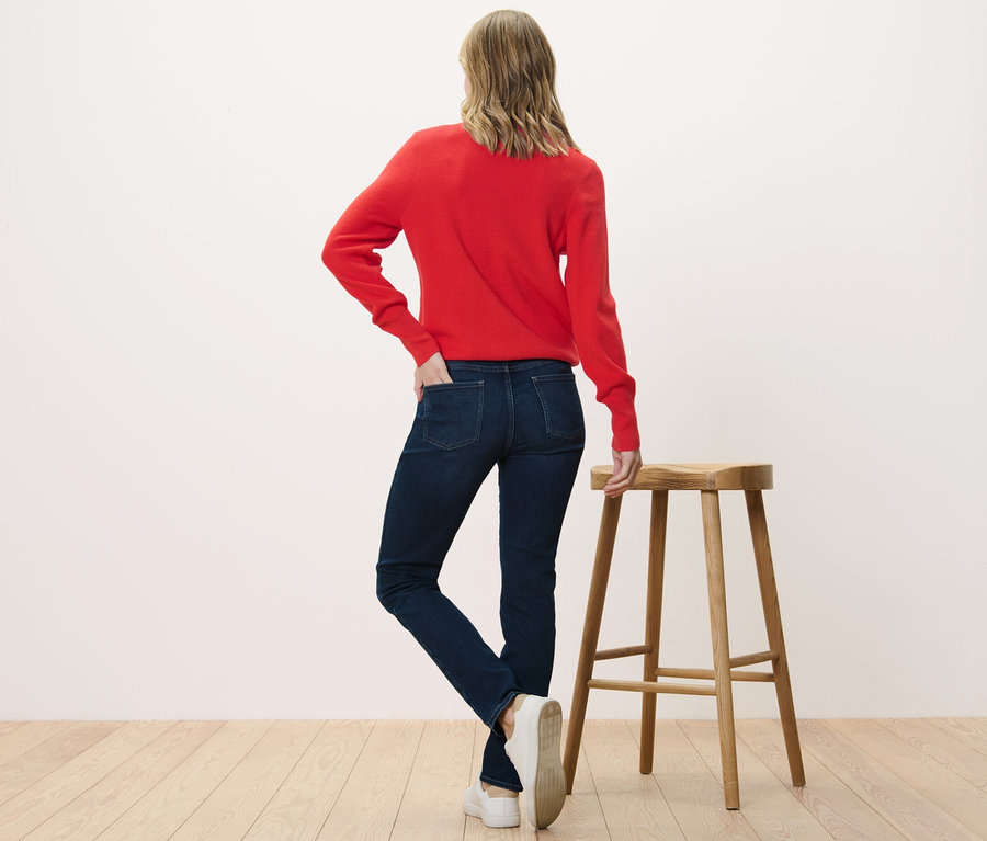Žena stojí chrbtom k fotoaparátu a má na sebe slim džínsy – strih »Emma« a červený sveter.