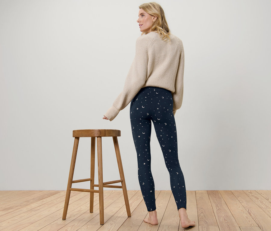 Žena stojí chrbtom k fotoaparátu a má na sebe mäkučké legínsy s potlačou hviezd a mesiacov.
