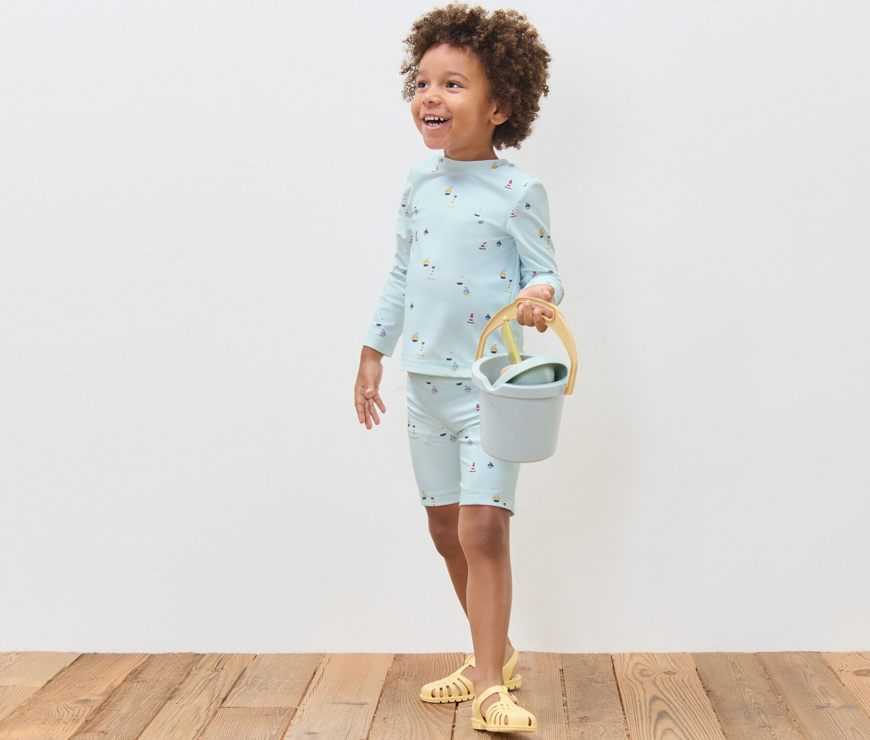 Chlapec v detskej súprave s UV faktorom 80 s námorníckym motívom drží vedierko a lopatku.