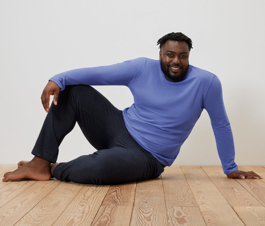 Muž sedí na drevenej podlahe v modro-tmavomodrom pyžame.