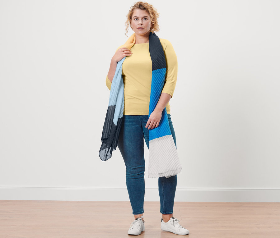 Žena pózuje v žltom tričku s 3/4 rukávom, tregínsoch »Fit Nelly« a s plisovanou šálou.