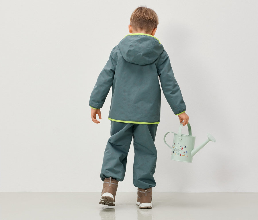 Chlapec v bunde a nohaviciach s kapucňou drží kanvicu.