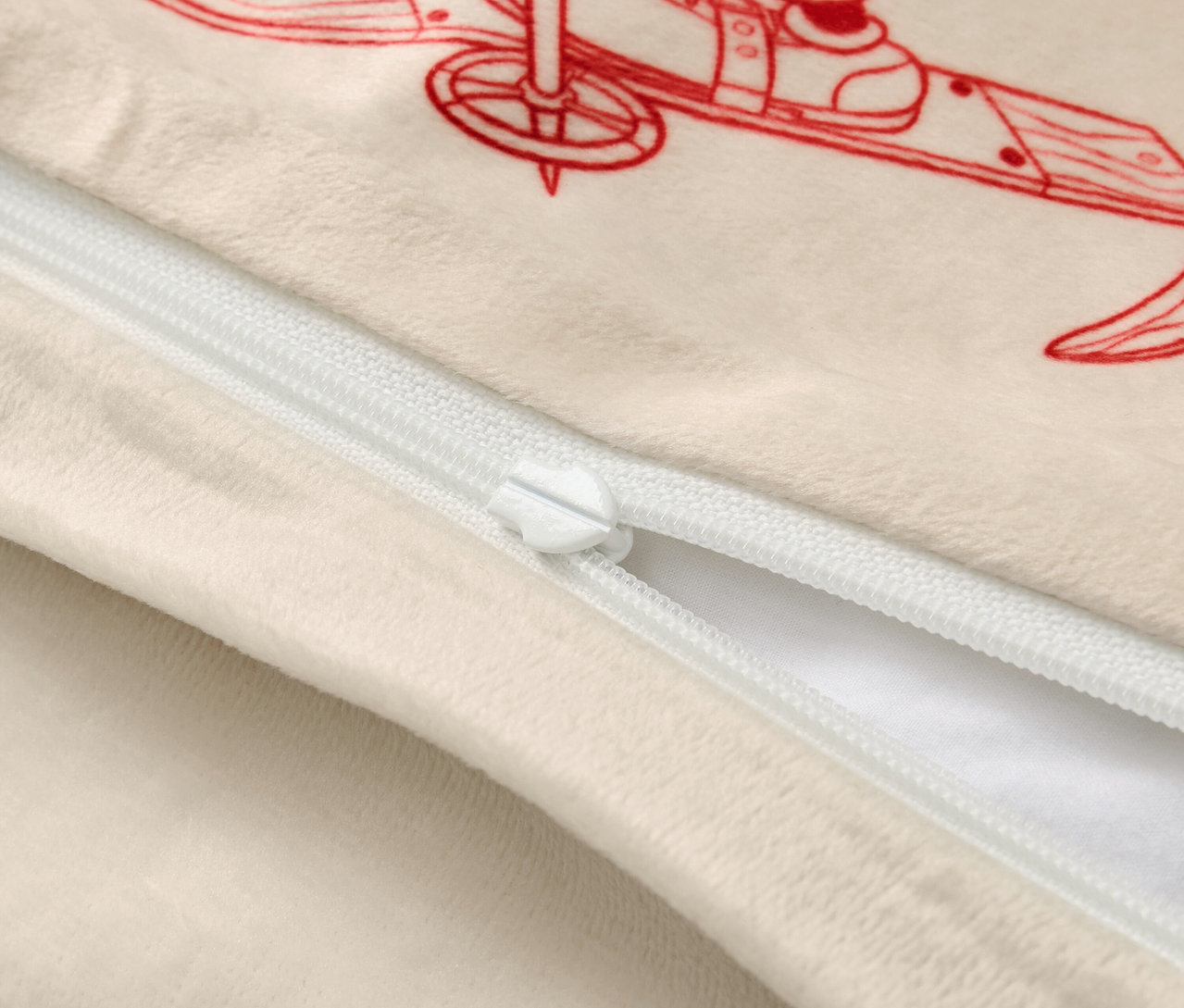 Béžová obliečka na vankúš s červenou ilustráciou lyžiara a bielym zipsom.