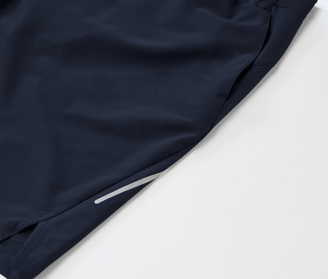 Detail tmavomodrých športových šortiek s vreckom a reflexným prvkom na nohavici.