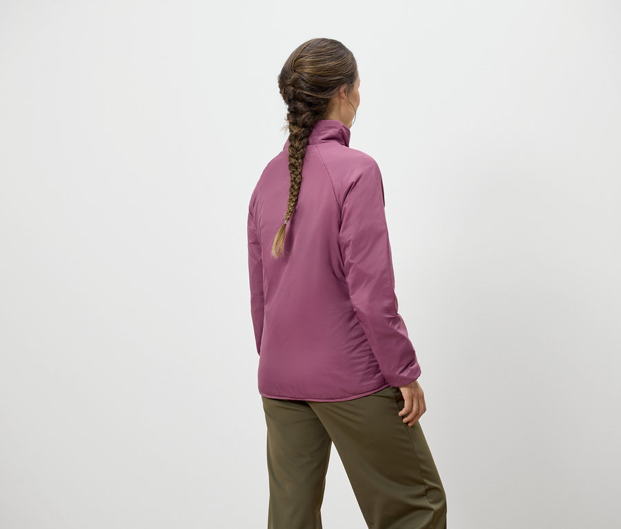 Žena s vrkočom stojí chrbtom a má na sebe ružovú bundu a zelené nohavice.