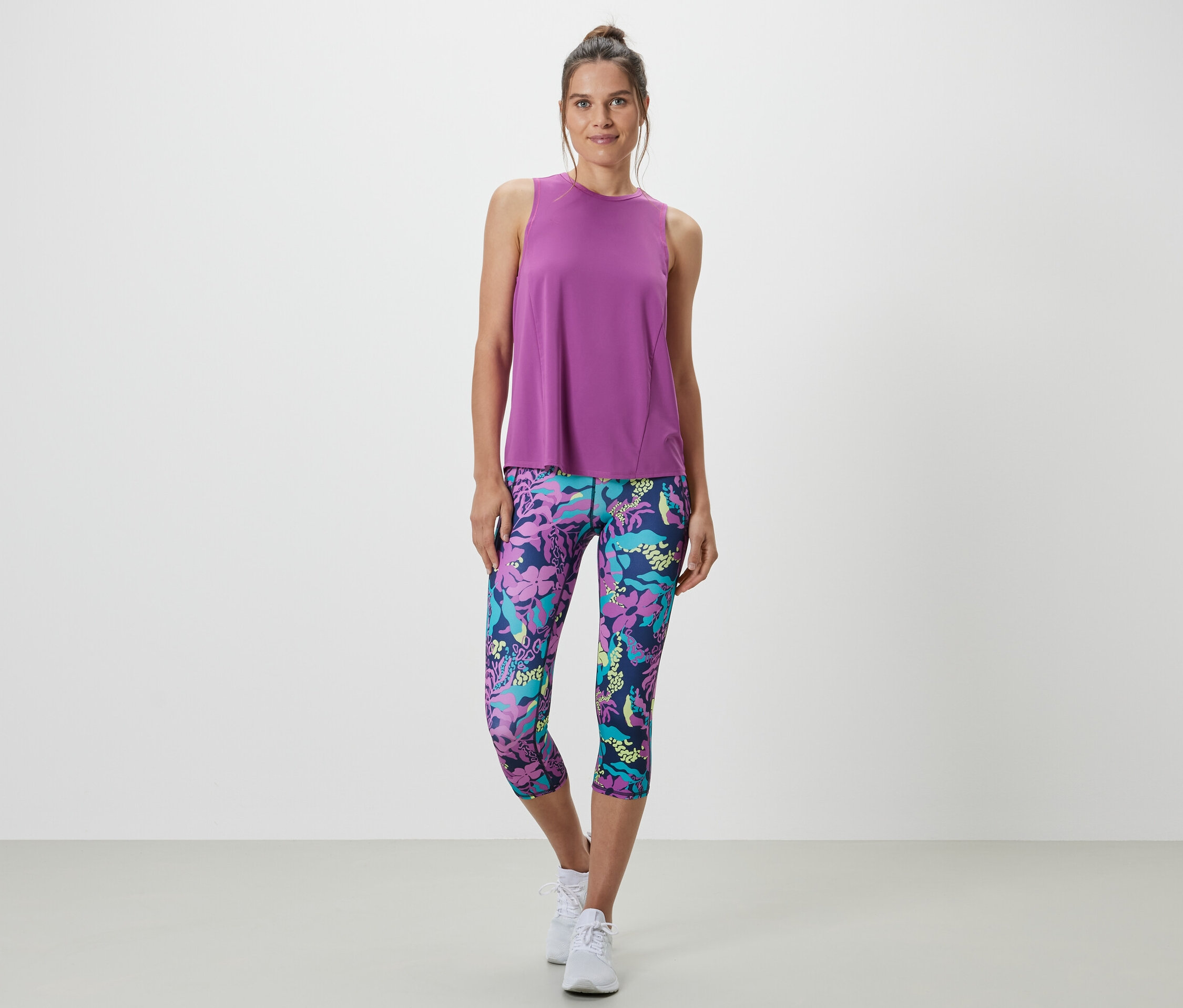 Žena má na sebe tyrkysový športový top z dvojdielnej súpravy a legíny s kvetinovou potlačou.