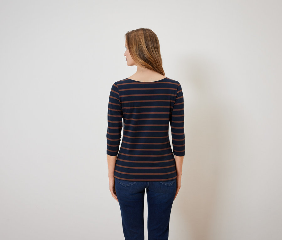 Pohľad zozadu na ženu v modro-hnedom pruhovanom tope a modrých džínsoch.