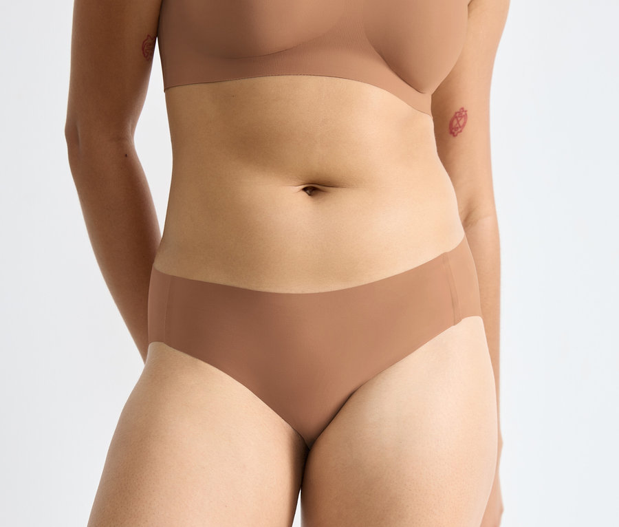 Žena má na sebe hnedú podprsenku a hnedé nohavičky sloggi ZERO Feel 2.0 High leg.