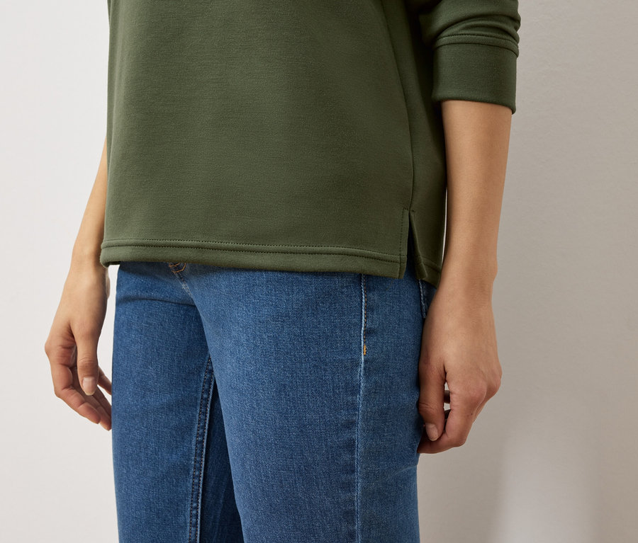 Trup ženy v olivovozelenej mikine a modrých džínsoch.