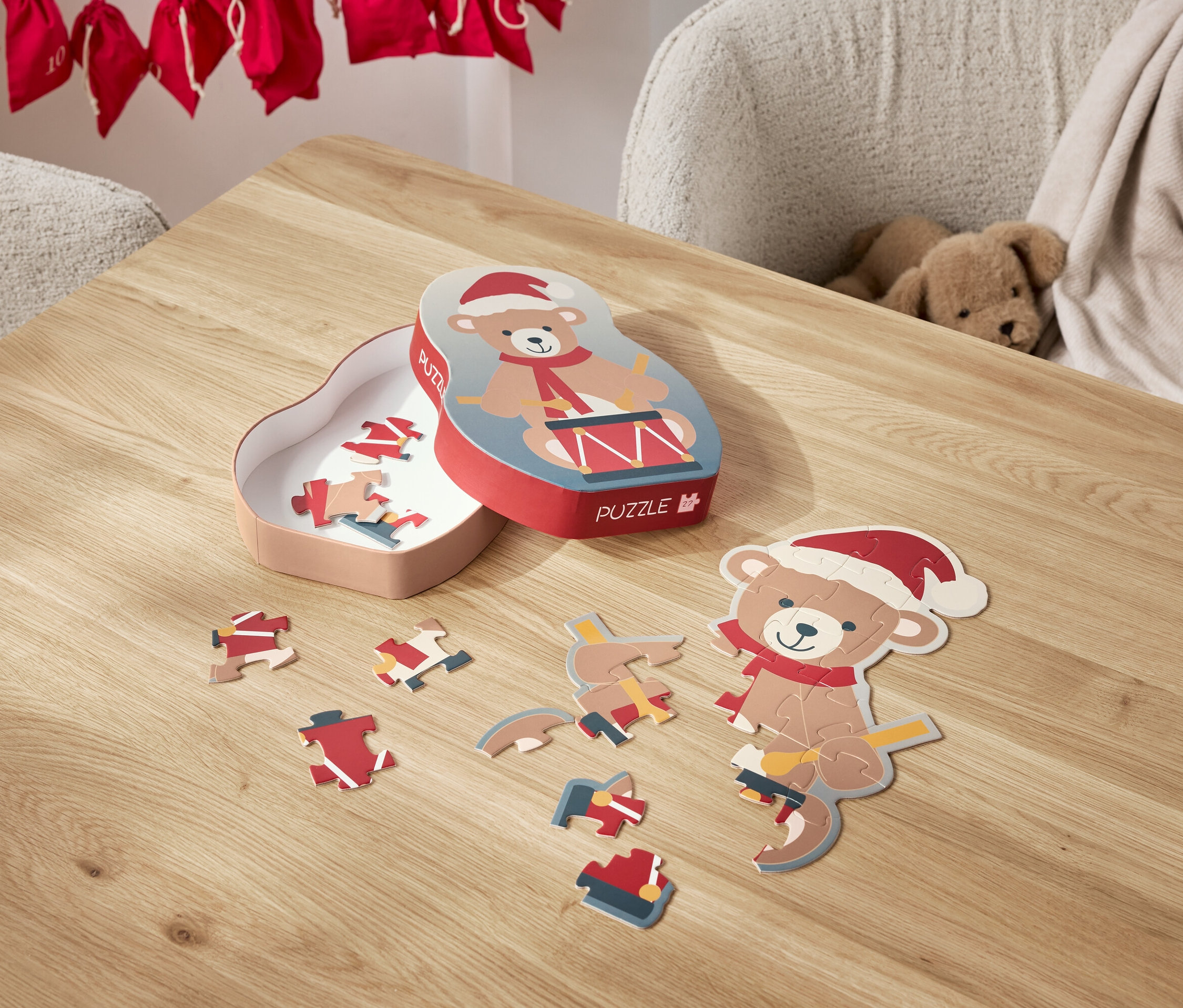 Na stole leží rozložené puzzle s motívom medvedíka v santovskej čiapke a jeho krabička.