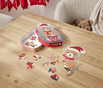Na stole leží rozložené puzzle s motívom medvedíka v santovskej čiapke a jeho krabička.