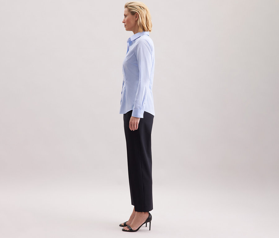 Žena stojí bokom a má na sebe svetlomodrú blúzku Seidensticker Slim Fit non iron.
