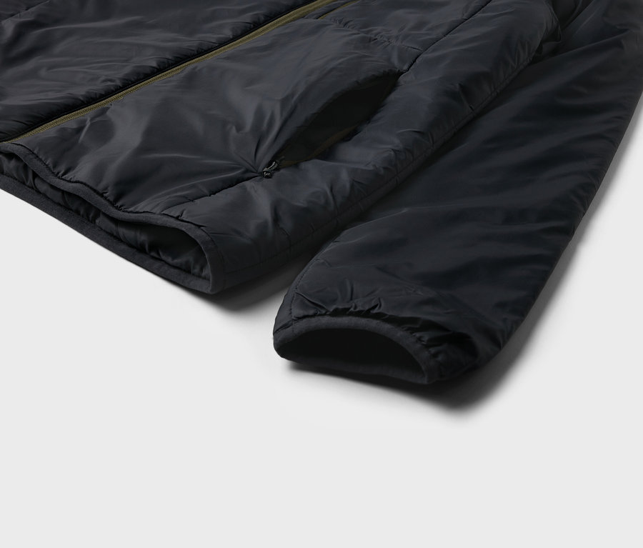 Detail čiernej bundy s vreckom a rukávom na svetlom pozadí.