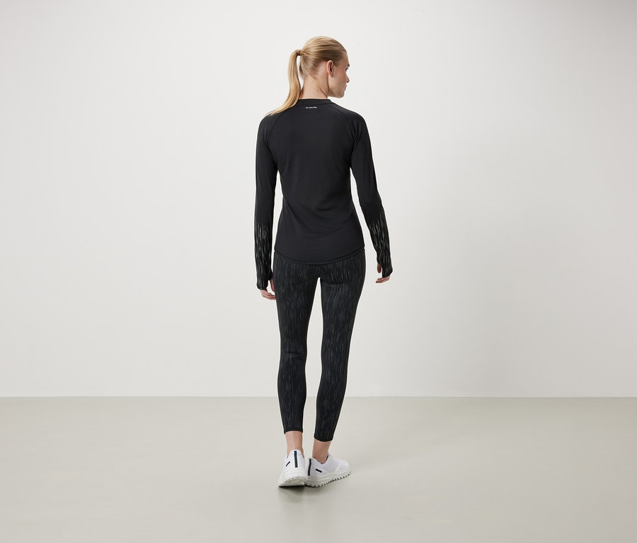 Žena chrbtom k fotoaparátu má na sebe čierne tričko s dlhým rukávom a vzorované legíny.