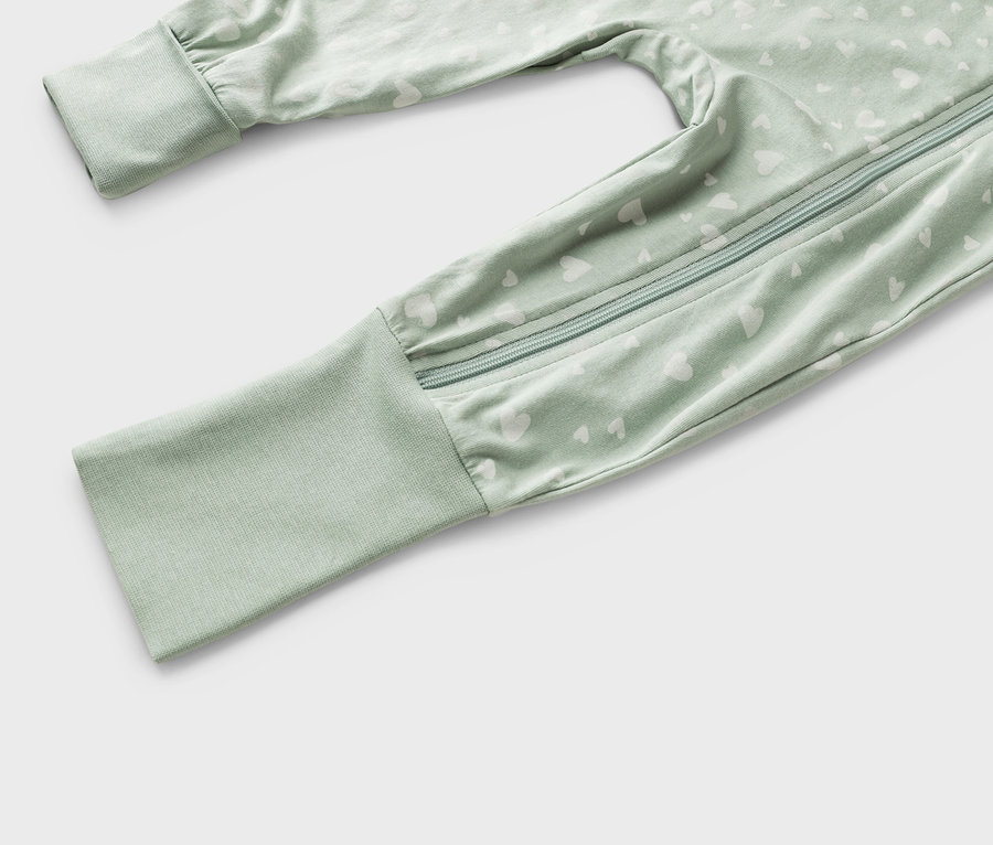 Detailný záber svetlozeleného detského overalu s bielym vzorom srdca a zipsom.