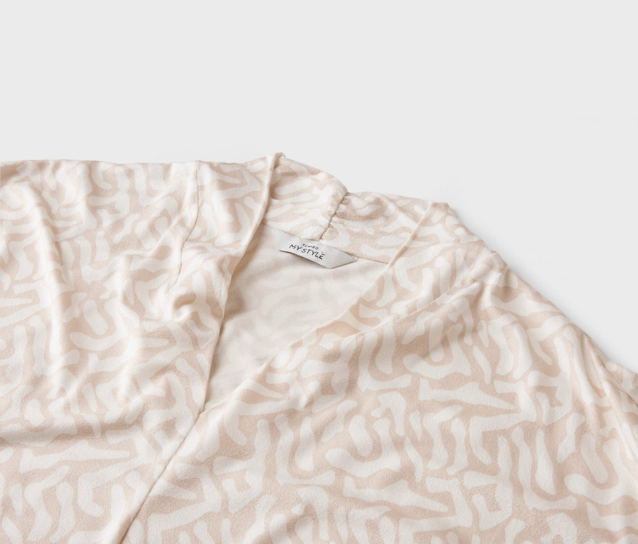 Detail záber svetlého kabáta s abstraktným vzorom a štítkom 'MY STYLE'.