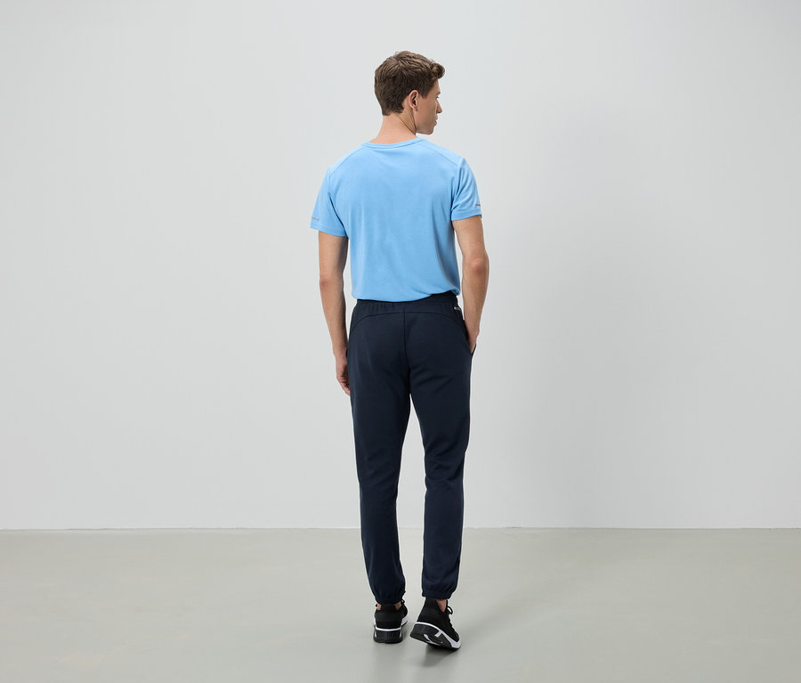 Muž stojí chrbtom k fotoaparátu, má na sebe svetlomodré tričko a tmavomodré nohavice.