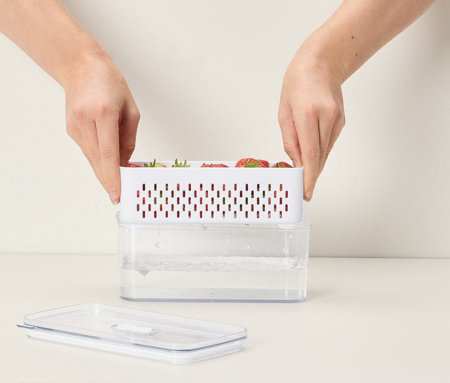 Ruky umiestňujú bielu nádobu s jahodami na priehľadnú nádobu s vodou.