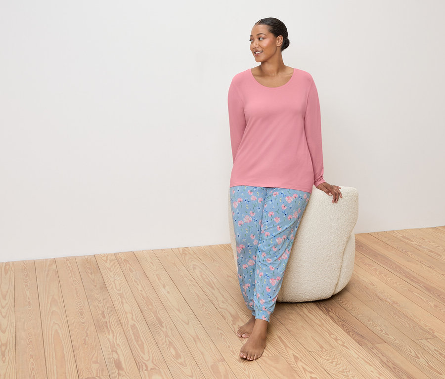 Žena v ružovom tope a modrých kvetinových nohaviciach sa opiera o béžový puf.