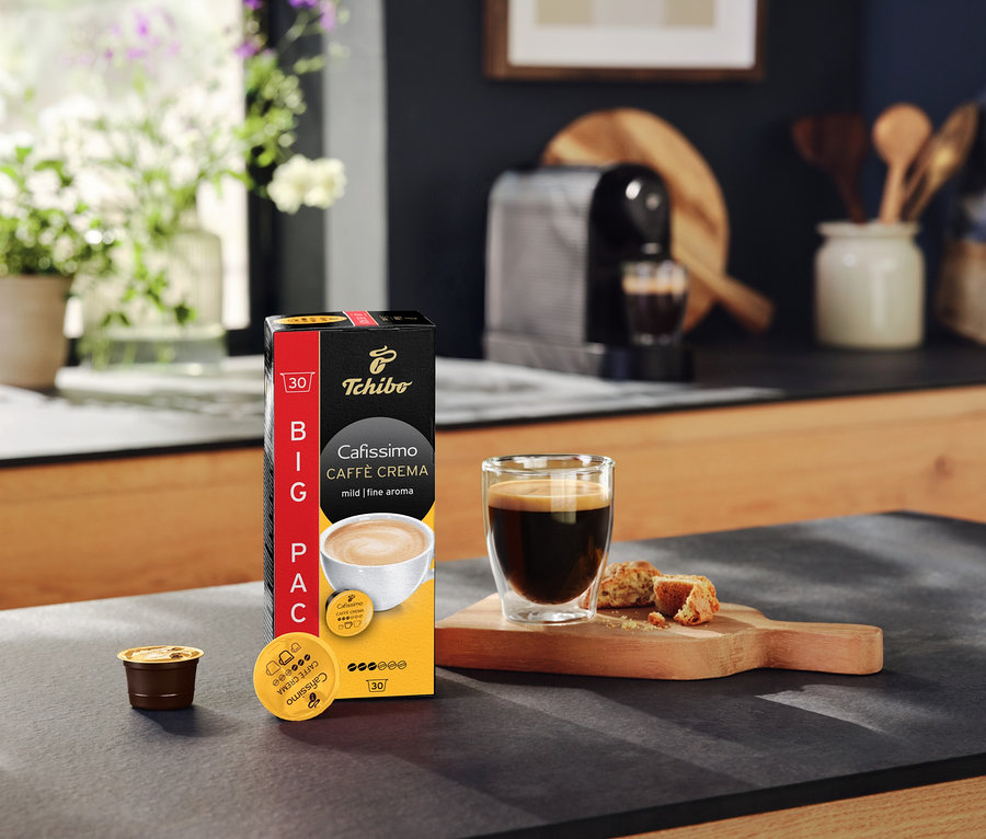 Balenie kapsúl Cafissimo Caffè Crema mild, šálka kávy a kávovar na kuchynskej linke.