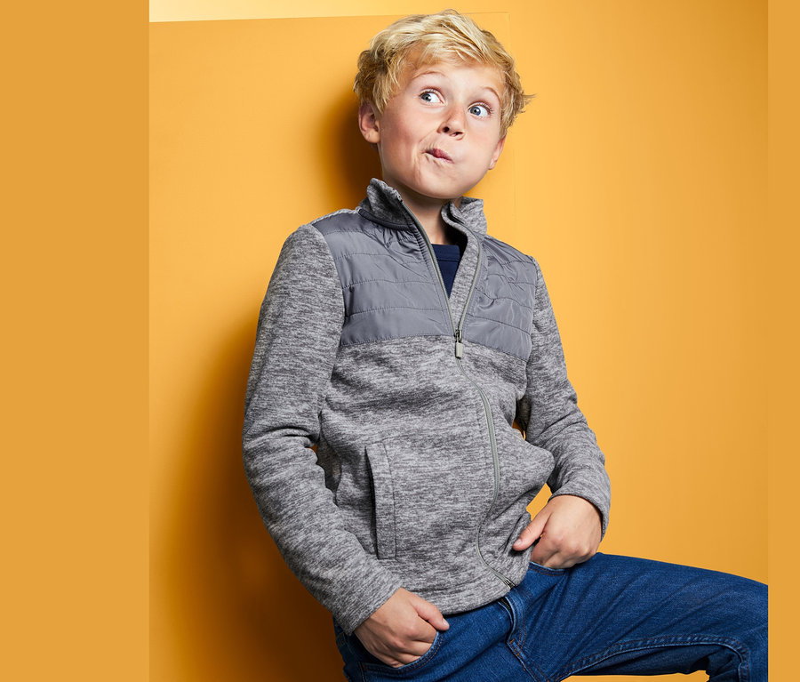 Chlapec pózuje v hybridnej flísovej bunde pred žltým pozadím.