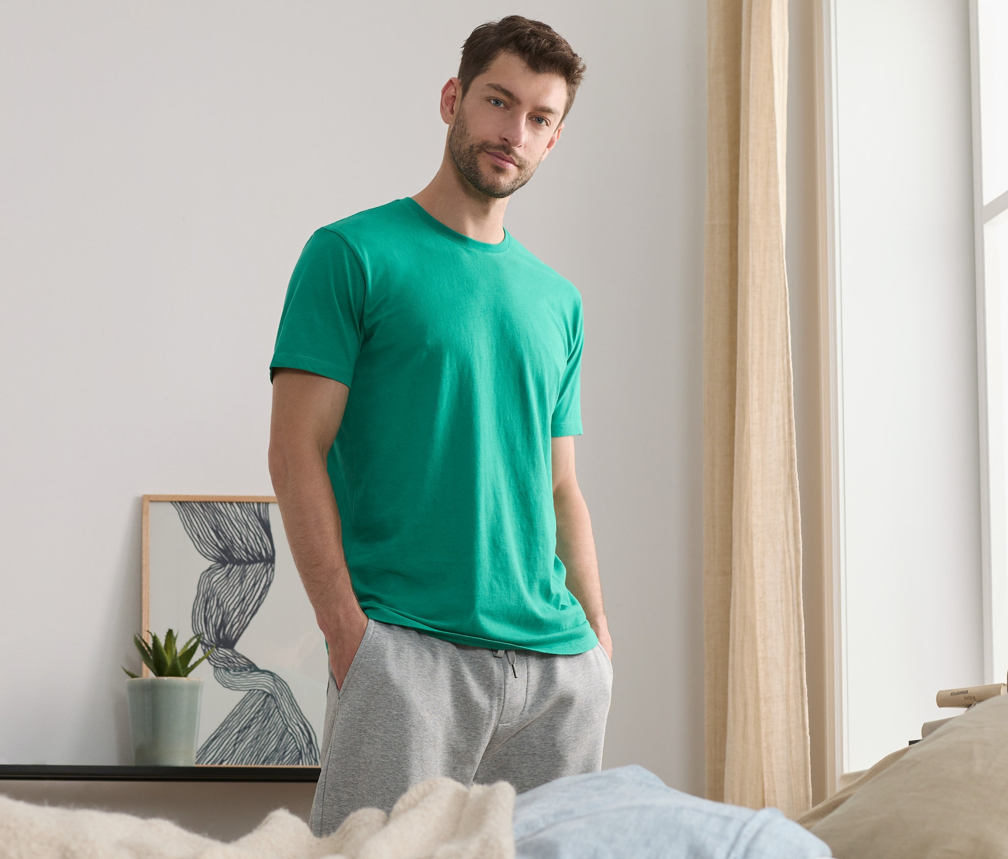 Muž pózuje v zelenom tričku s okrúhlym výstrihom (2 ks) a sivých teplákoch.