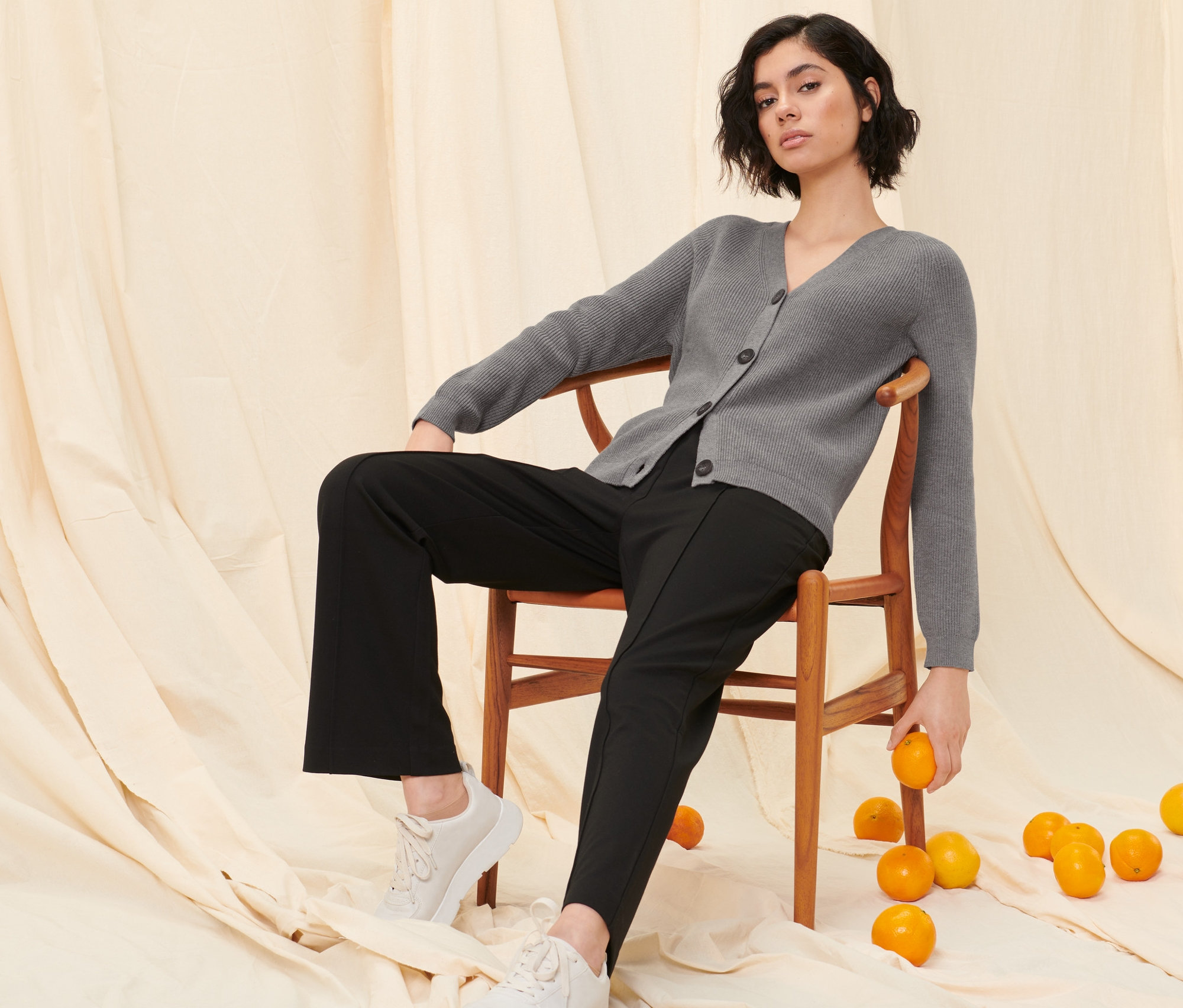 Žena sedí na stoličke v šedom hrubom kardigáne a čiernych teplákových nohaviciach.