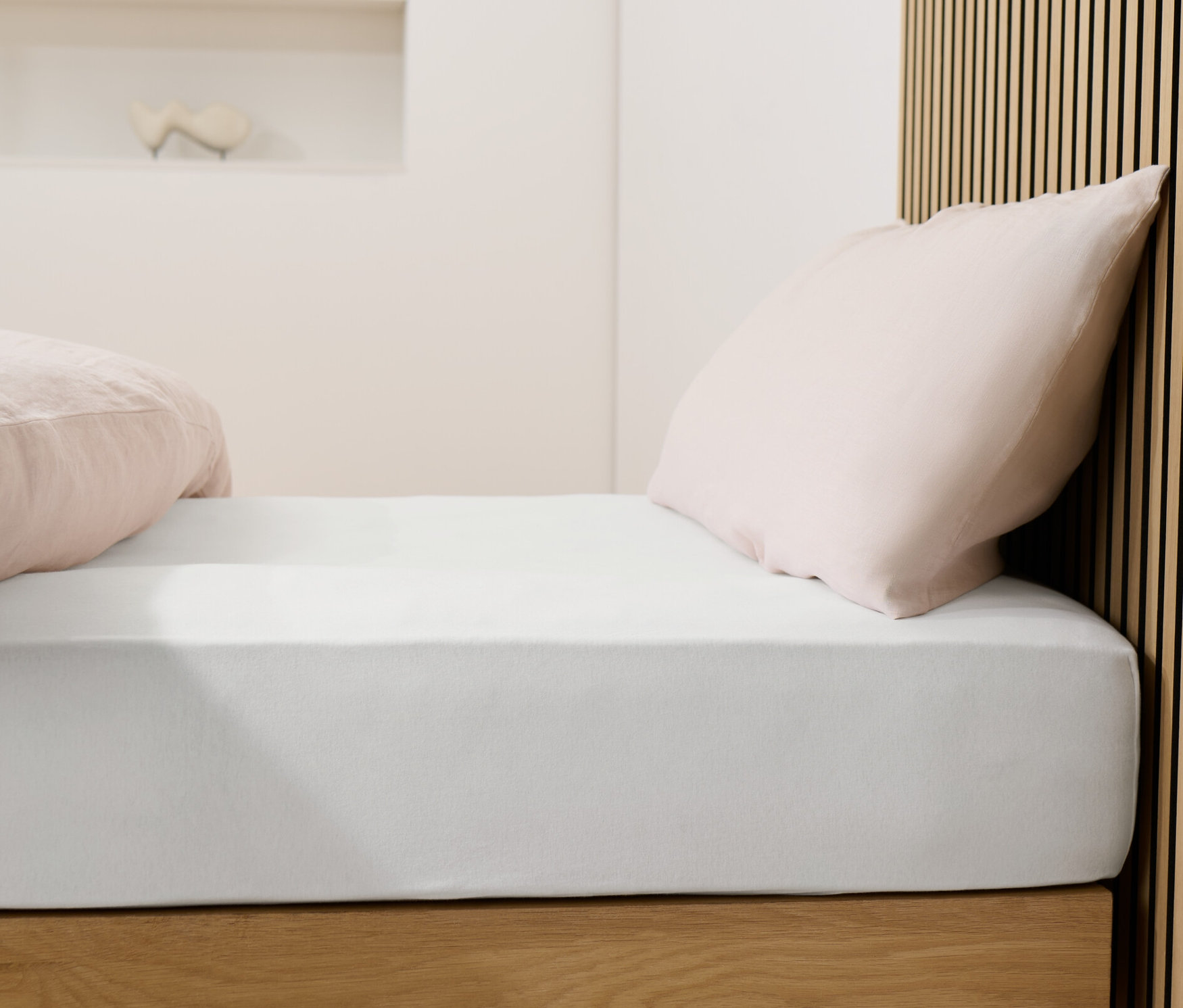 Posteľ s bielou džersejovou plachtou a ružovými vankúšmi.