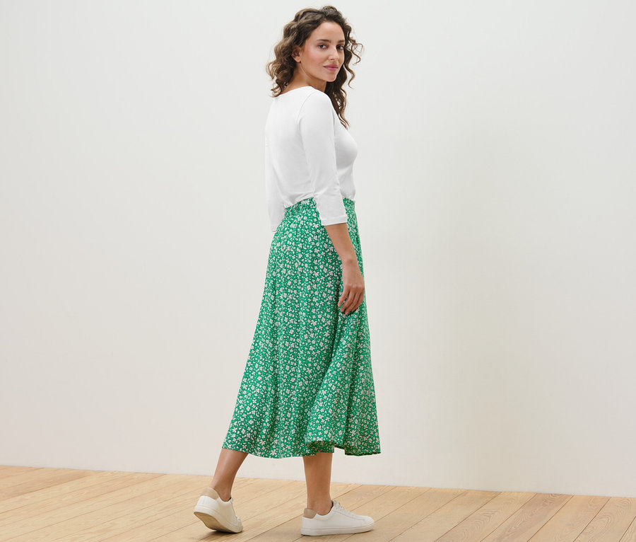 Žena pózuje v zelenej midi sukni s potlačou a bielom tope.