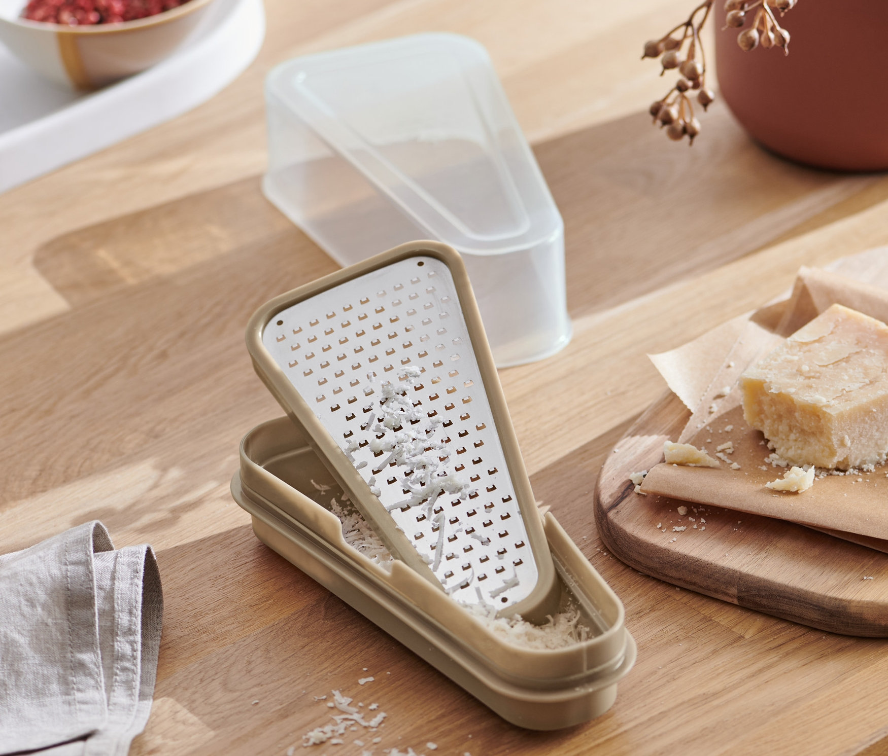 Pohľad zhora na strúhadlo na parmezán 2 v 1 s nádobou na drevenom stole spolu s jedlom.