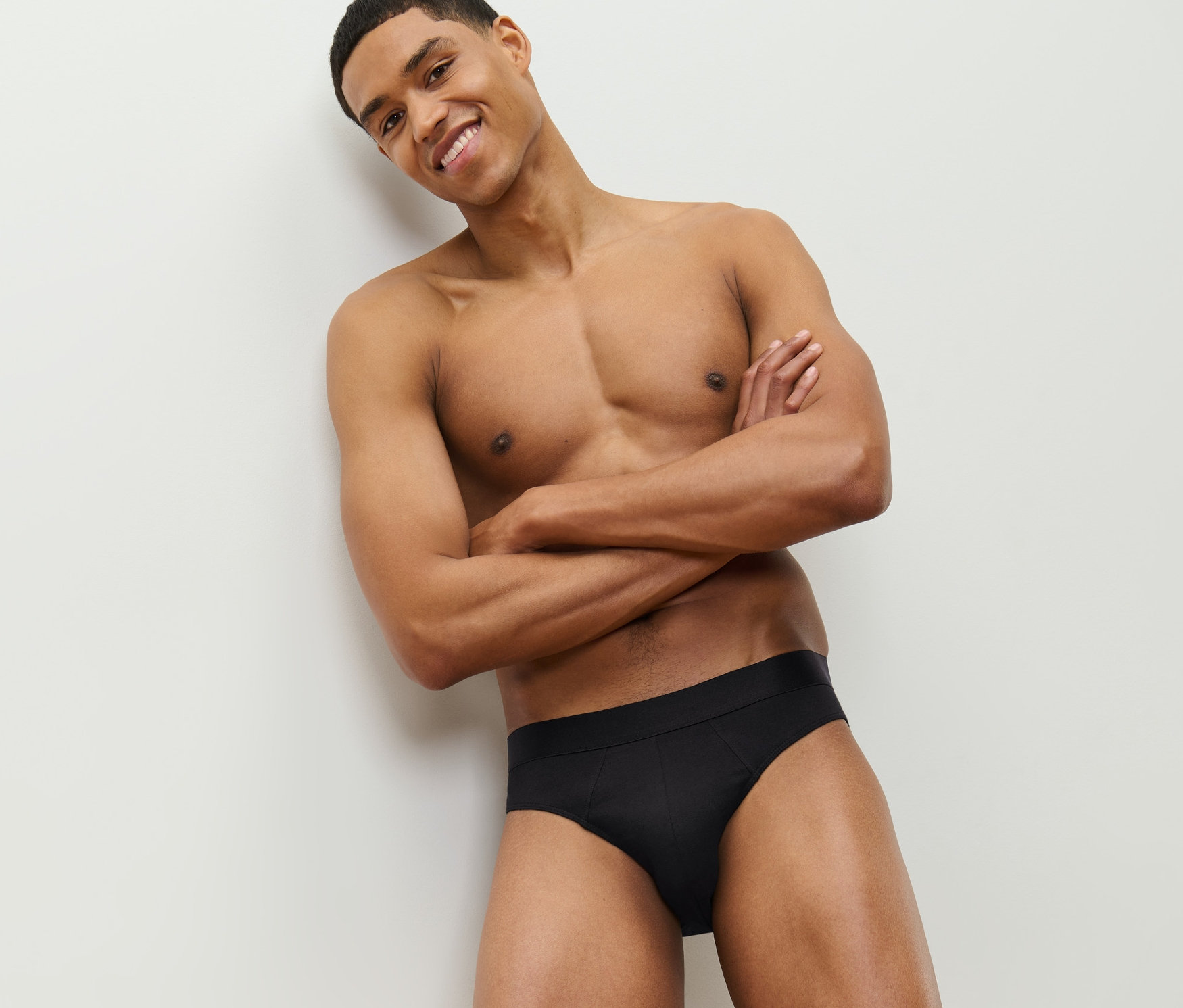 Usmievajúci sa muž pózuje so skríženými rukami na hrudi a má na sebe čierne slipy, 4 ks.